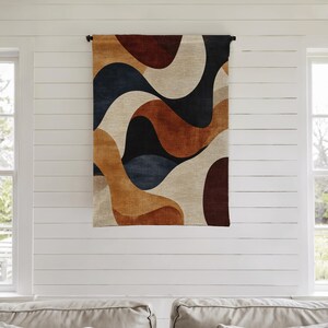 Pu&ograve; includere: Un arazzo rettangolare con un design astratto. Il motivo presenta forme fluide nei toni del marrone, beige, blu navy e nero. L'arazzo &egrave; sospeso a un'asta nera contro un muro bianco.