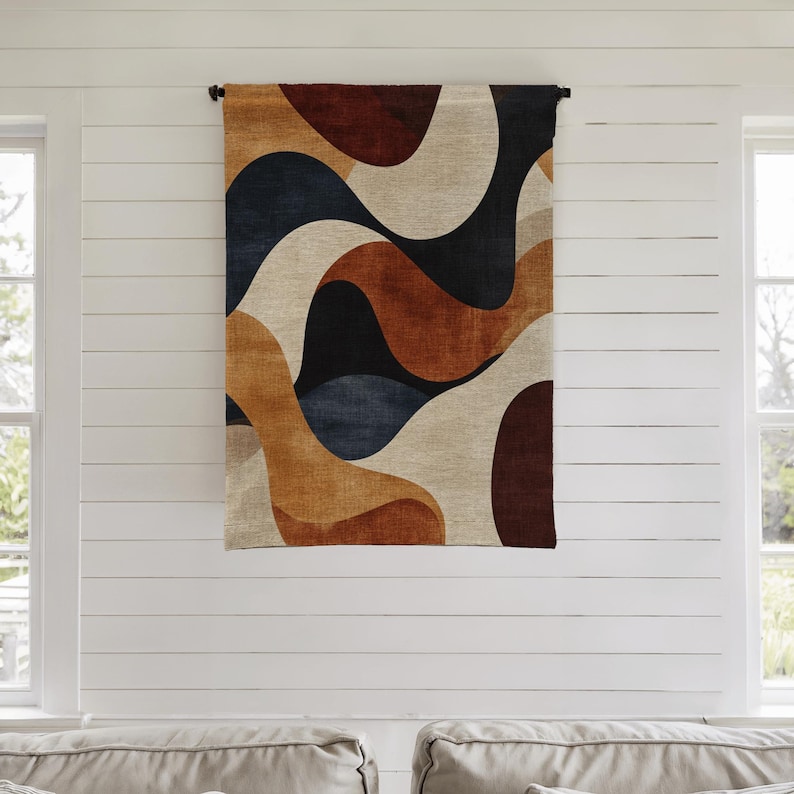 Pu&ograve; includere: Un arazzo rettangolare con un design astratto. Il motivo presenta forme fluide nei toni del marrone, beige, blu navy e nero. L'arazzo &egrave; sospeso a un'asta nera contro un muro bianco.