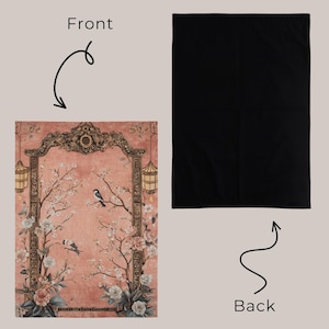 May include: A rectangular, peach-colored blanket with a floral and bird design. The front features a detailed illustration of cherry blossoms, birds, and ornate architectural elements. The back is solid black.