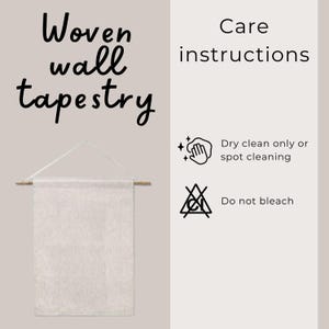 May include: A woven wall tapestry with a cream-colored fabric, suspended from a wooden dowel and white string. The image includes care instructions: dry clean only or spot cleaning, and do not bleach.