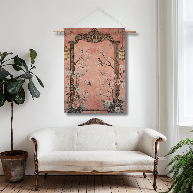 May include: A wall hanging featuring a vintage-style design with a pink background. The artwork includes a decorative frame, floral elements, birds, and lanterns. The piece is suspended from a wooden rod.