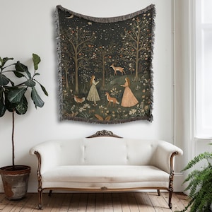 Op de afbeelding: Een wandtapijt met een bossc&egrave;ne met twee vrouwen, herten en vossen. Het kunstwerk heeft een donkere achtergrond met bomen, bloemen en een halve maan. Het wandtapijt heeft een gefranjerde rand en hangt aan een muur.