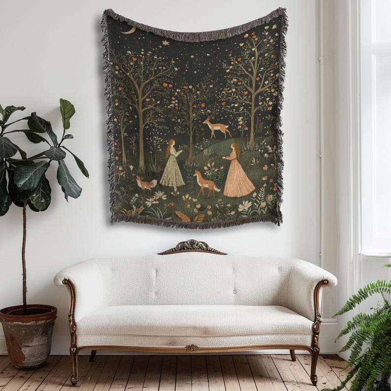 Op de afbeelding: Een wandtapijt met een bossc&egrave;ne met twee vrouwen, herten en vossen. Het kunstwerk heeft een donkere achtergrond met bomen, bloemen en een halve maan. Het wandtapijt heeft een gefranjerde rand en hangt aan een muur.