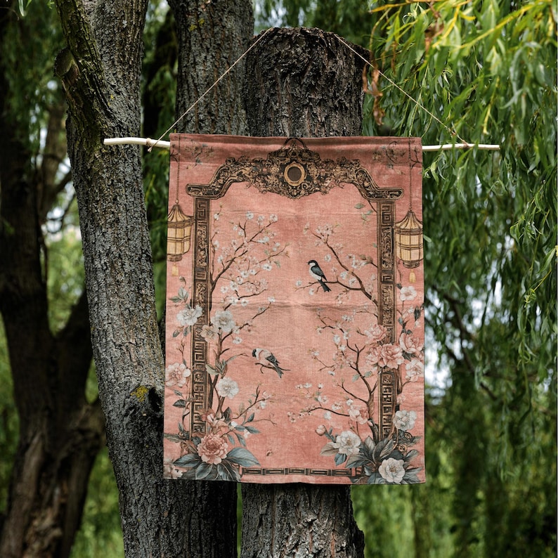 May include: A decorative wall hanging with a pink background, featuring a floral and bird design. The artwork includes blossoming branches, birds, and ornate framing with lanterns. The hanging is suspended from a wooden rod.