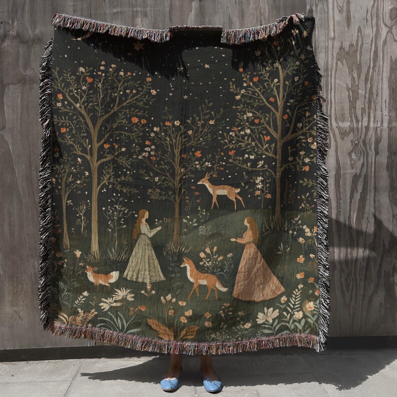 Op de afbeelding: Een donkergroene geweven sprei met een bossc&egrave;ne met bomen, herten, vossen en figuren in lange jurken. De deken heeft een franjerand en een gedetailleerde illustratie met een sterrenhemel.