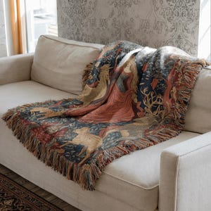 Pu&ograve; includere: Una coperta tessuta con un design dettagliato in stile arazzo, raffigurante una figura centrale in abito rosso, un unicorno e vari animali su uno sfondo floreale blu scuro, rifinita con frange decorative lungo i bordi.