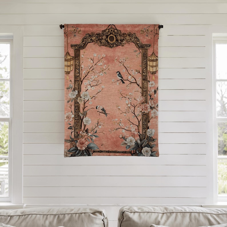 May include: A decorative wall tapestry featuring a peach-colored background with a floral and bird design. The tapestry has a dark brown ornate frame with lanterns on each side. The design includes white and pink flowers and two birds perched on branches.
