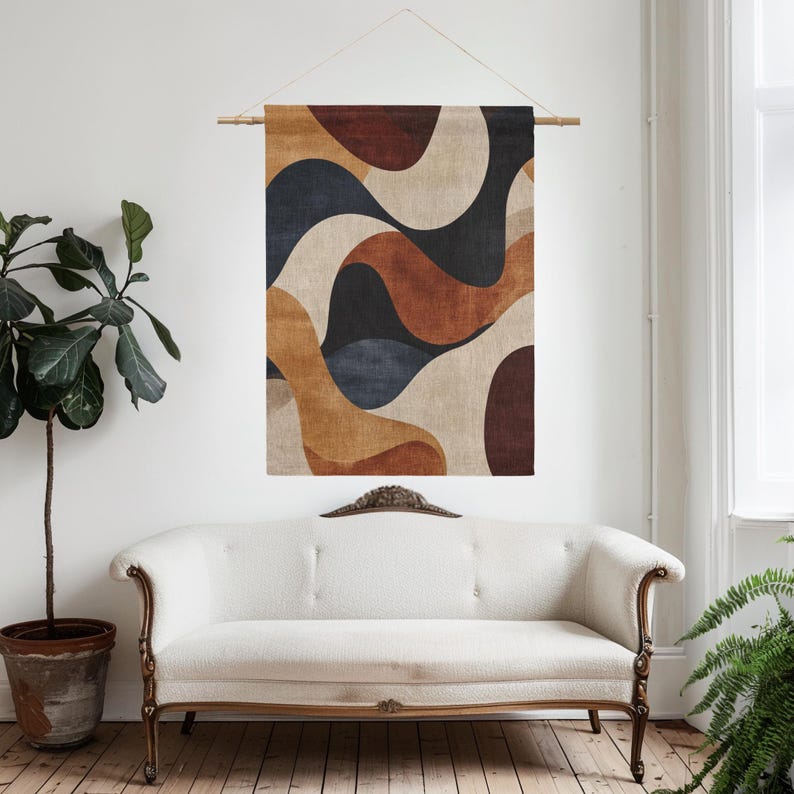 Pu&ograve; includere: Un arazzo da parete con un design astratto. L'opera presenta forme organiche fluide in tonalit&agrave; di marrone, beige, blu navy e nero. &Egrave; sospeso a un'asta di legno con un cordino naturale. L'arazzo &egrave; esposto sopra un divano bianco.