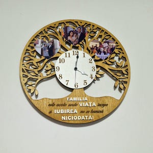 Puede incluir: Un reloj de madera con forma de árbol con tres marcos de fotos en forma de corazón. La esfera del reloj es blanca con números y manecillas negras. El texto en el reloj dice "FAMILIA este acolo unde VIAŢA incepe si IUBIREA nu se termină NICIODATÀI".