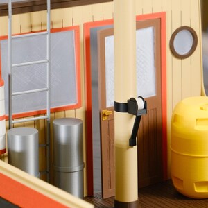May include: A detailed model of a boat's interior, featuring a yellow and orange color scheme. The model includes a ladder, windows, a door, and a cylindrical yellow structure. The design is reminiscent of a tugboat or similar vessel.