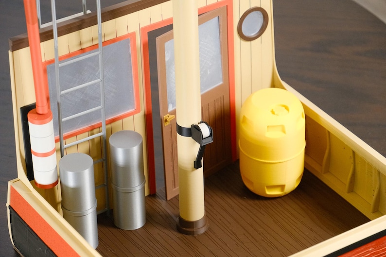 May include: A toy boat deck featuring a cream-colored wall with a brown door, a silver ladder, and a central mast. Two silver cylindrical canisters stand near the ladder, while a bright yellow barrel sits on the brown wood-grain floor.