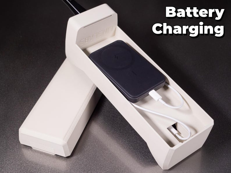 May include: A white plastic phone-shaped charging dock with a black wireless charging pad inside. The charging pad is connected to a white charging cable. The text "Battery Charging" is visible in the upper right corner of the image.