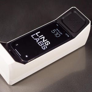 May include: A white phone-shaped device with a black smartphone inside. The smartphone screen displays the time 5:10 and the text "LINS LABS".
