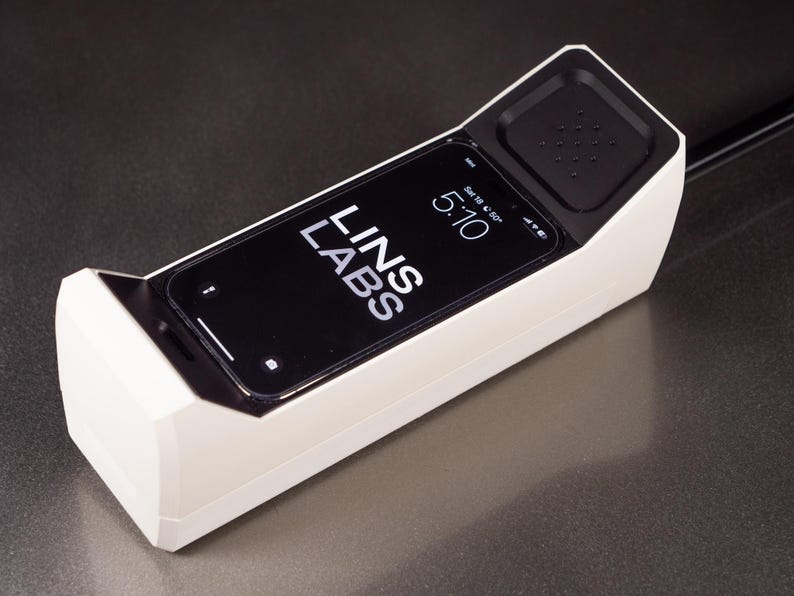 May include: A white phone-shaped device with a black smartphone inside. The smartphone screen displays the time 5:10 and the text "LINS LABS".