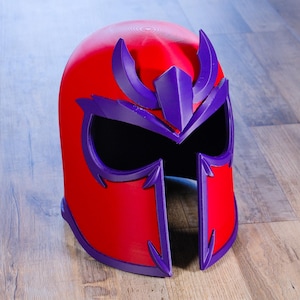 May include: A bright red helmet featuring a prominent purple trim and a stylized purple crest on the forehead. The helmet has a wide, open face opening with a sharp, angular design around the eye area and a smooth, rounded top surface.