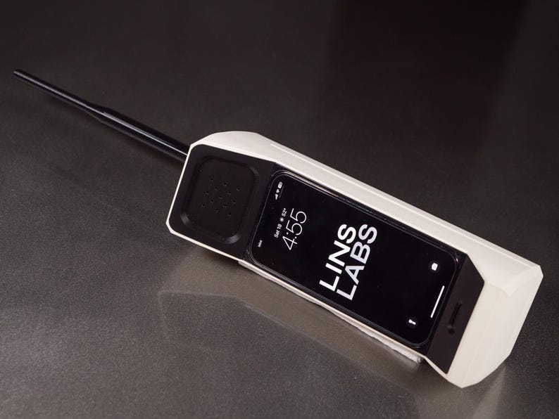 May include: A white retro-style phone with a black antenna and a black screen displaying the time 4:55 and the text "LINS LABS".