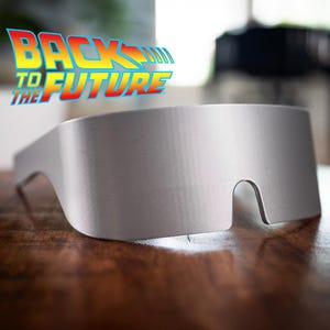 Può includere: Un paio di occhiali da sole futuristici color argento con un design unico. Gli occhiali sono su una superficie di legno.