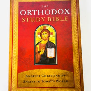May include: The cover of a red book titled "The Orthodox Study Bible" with a gold border and a picture of Jesus Christ in the centre. The text below the title reads "Ancient Christianity Speaks to Today's World."