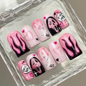 Könnte beinhalten: Ein Set aus zehn künstlichen Fingernägeln mit hellrosa Basis und verschiedenen Motiven, darunter schwarz-rosa Flammen, rosa Herzen, weiße Telefonsymbole mit dem Text CALL ME sowie eine rosa-schwarze Geistermaske mit kleinen weißen Kreuzen.
