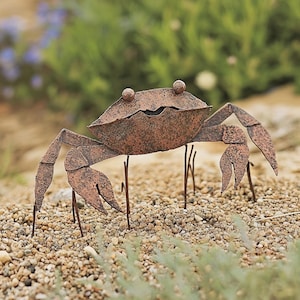May include: A rusty metal crab sculpture with long legs and a detailed shell. The crab is standing on a bed of small brown rocks.