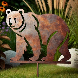Puede incluir: Una estaca de jardín de metal oxidado con la silueta de un oso. El oso está de pie en un césped verde.