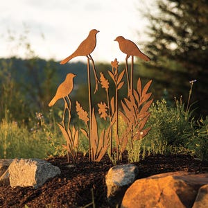 May include: Metal garden art sculpture featuring three birds perched on tall stalks with stylized leaves and flowers. The sculpture is rusted brown and has a rustic look.