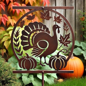 Puede incluir: Una estaca de jardín de metal con un diseño recortado de un pavo y calabazas. La estaca es marrón y tiene un aspecto rústico. El pavo está mirando hacia la derecha y tiene un diseño detallado. Las calabazas están a ambos lados del pavo y también están detalladas.