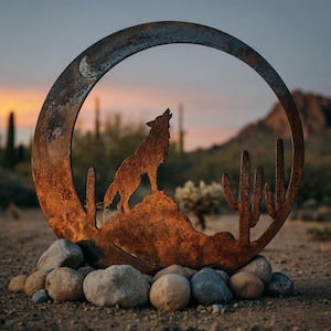 May include: A weathered metal sculpture depicting a howling wolf within a crescent moon and desert scene. The sculpture has a rusty brown finish and is set on a base of stones. The background shows cacti and a sunset, evoking a sense of the American Southwest.
