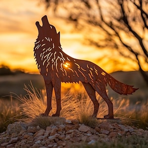 May include: A rusty metal wolf sculpture in a howling pose, set against a sunset. The sculpture is placed on a small pile of rocks and grass. The wolf's body has cut-out details, and the background is a warm orange and yellow.