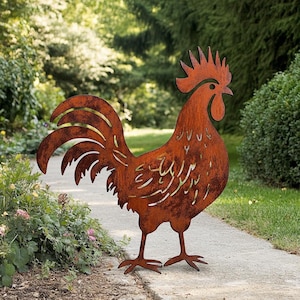 May include: A large, rusty-orange metal rooster garden sculpture stands on a concrete path. The rooster has a detailed silhouette with cut-out feather designs and a prominent comb. The sculpture is placed in a garden setting with greenery in the background.