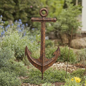 Könnte beinhalten: Ein rostiger Anker-Gartenpfahl aus Metall mit dekorativem Design. Der Anker steht aufrecht in einem Garten.