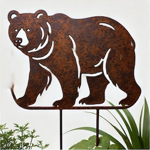 Puede incluir: Una estaca de jardín de metal marrón oxidado en forma de silueta de oso. El oso camina hacia la derecha. La estaca está diseñada para ser colocada en el suelo.