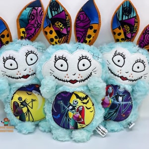 Może przedstawiać: Trzy niebieskie pluszowe zabawki w kształcie królika z kolorowymi uszami w patchworku. Każdy królik ma białą twarz z haftowanymi detalami i inny bohater z filmu Koszmar przed świętami na przodzie.