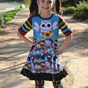 Puede incluir: Una niña con un vestido azul con un diseño de búho y una falda con personajes de dibujos animados. El vestido tiene mangas a rayas y un volante negro en el dobladillo. También lleva leggings estampados.