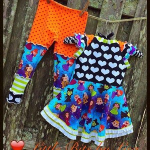 May include: A blue and purple dress with a white heart print and a ruffle trim. The dress is paired with orange leggings with white polka dots and a green and white striped cuff.