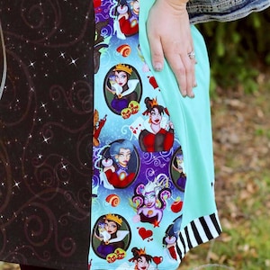 May include: A colourful dress featuring a black and teal pattern with various cartoon villain characters. The dress has a teal panel and a black and white striped hem. The Shady Pines Stitchery logo is visible.