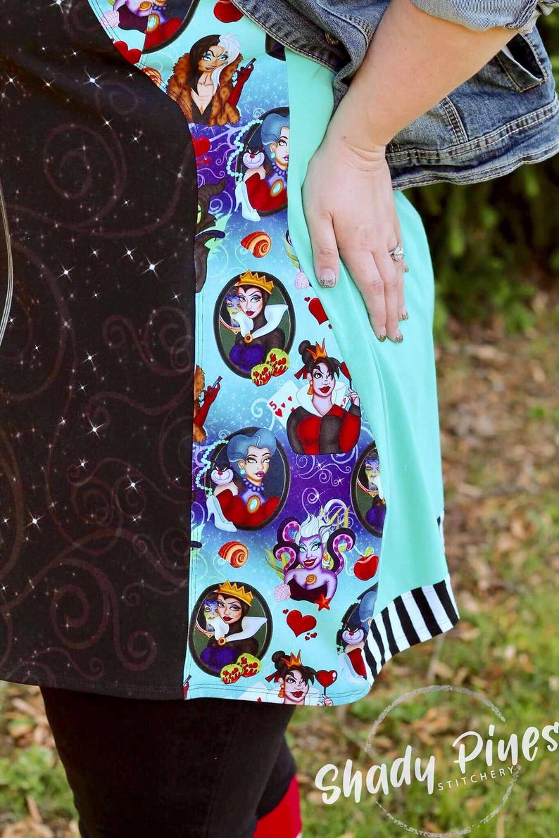 May include: A colourful dress featuring a black and teal pattern with various cartoon villain characters. The dress has a teal panel and a black and white striped hem. The Shady Pines Stitchery logo is visible.