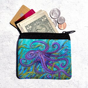 May include: A small zippered pouch with a colorful octopus design. The octopus is purple and blue with green seaweed and small blue fish. The pouch is open and has cash and credit cards inside.