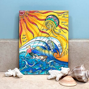 May include: A vibrant, hand-drawn canvas art piece depicts a surfer riding a wave under a bright sun and a kite. The artwork features a color palette of yellow, orange, blue, and white, with a detailed illustration style. The theme is surfing and beach life.