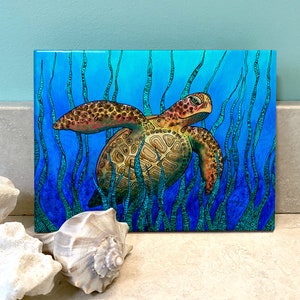 May include: A colorful illustration of a sea turtle swimming through a field of blue and green seaweed. The turtle has a brown shell with orange and yellow accents. The seaweed is detailed with intricate patterns.