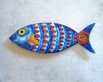 May include: A blue, pink, and yellow painted wooden fish with a whimsical design. The fish has a large eye and a detailed tail fin.