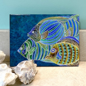 May include: A colorful painting of three fish on a blue background. The fish are stylized and have intricate patterns in shades of blue, green, and gold.