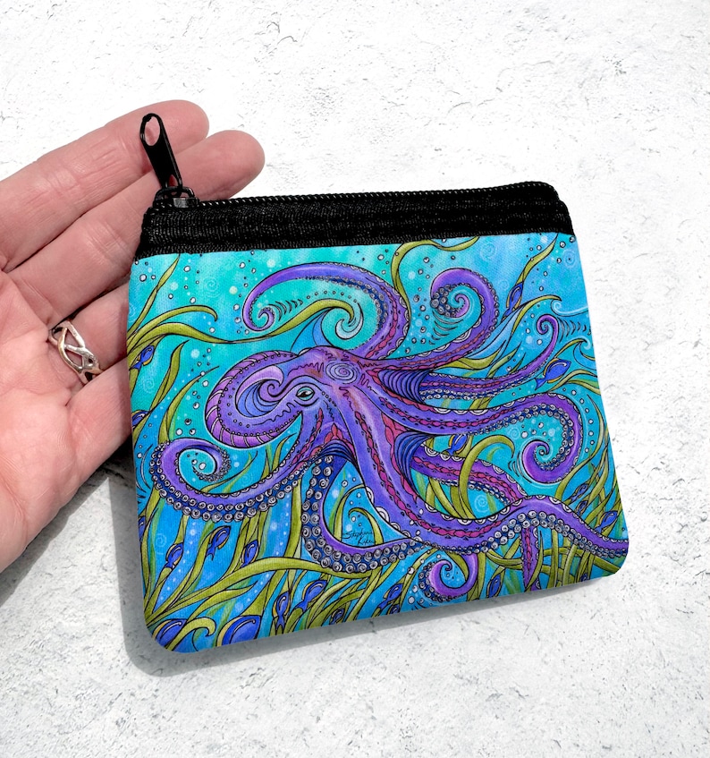 May include: A purple octopus with swirling tentacles is surrounded by green seaweed and blue fish on a turquoise background. The octopus is featured on a zippered pouch.