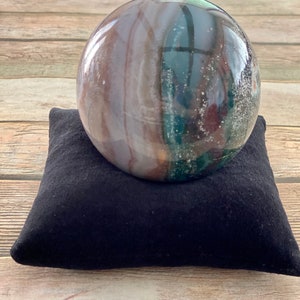 May include: A large, polished, green, brown, and white agate sphere on a black velvet cushion.