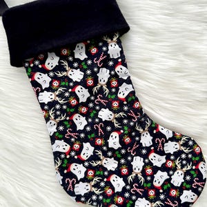 May include: A black Christmas stocking with a black cuff. The patterned fabric features white ghosts wearing Santa hats, reindeer, candy canes, snowflakes, and wrapped gifts on a dark background.