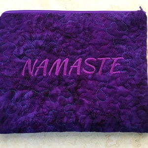 May include: Purple quilted zippered pouch with the word "NAMASTE" embroidered in pink.