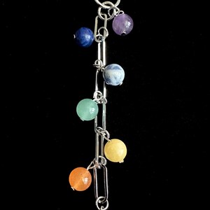 May include: A silver-toned keychain with a series of colorful gemstone beads. The beads are arranged in a vertical line, with colors including blue, purple, green, yellow, orange, and red. The keychain has a clasp at the top.