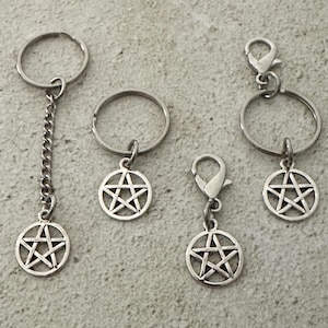 May include: A collection of silver-toned keychains and charms featuring a pentagram design. The keychains include a chain, split rings, and lobster clasps for attachment. The charms are circular with a five-pointed star in the center.