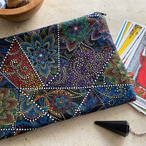 May include: A black fabric pouch with a colorful dot pattern design. The pouch is lying on a white surface next to a deck of tarot cards and a black pendulum.