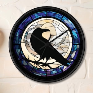 May include: A round wall clock with a black frame and a stained-glass design. The clock face features a black silhouette of a raven perched on a branch against a backdrop of blue, purple, and white glass. The clock hands are black.